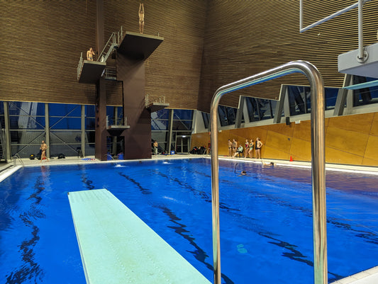 Indoor swimming pool with diving platform and swimmers in a modern building.