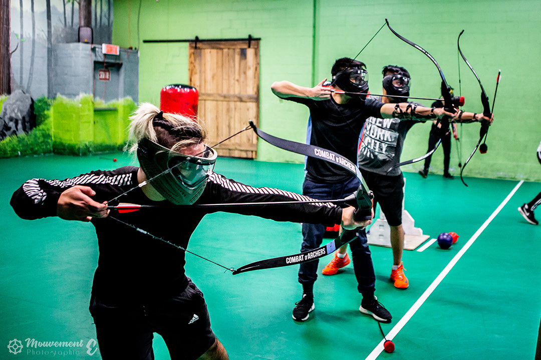 Group of people practicing archery in an indoor facility with green walls and floor.