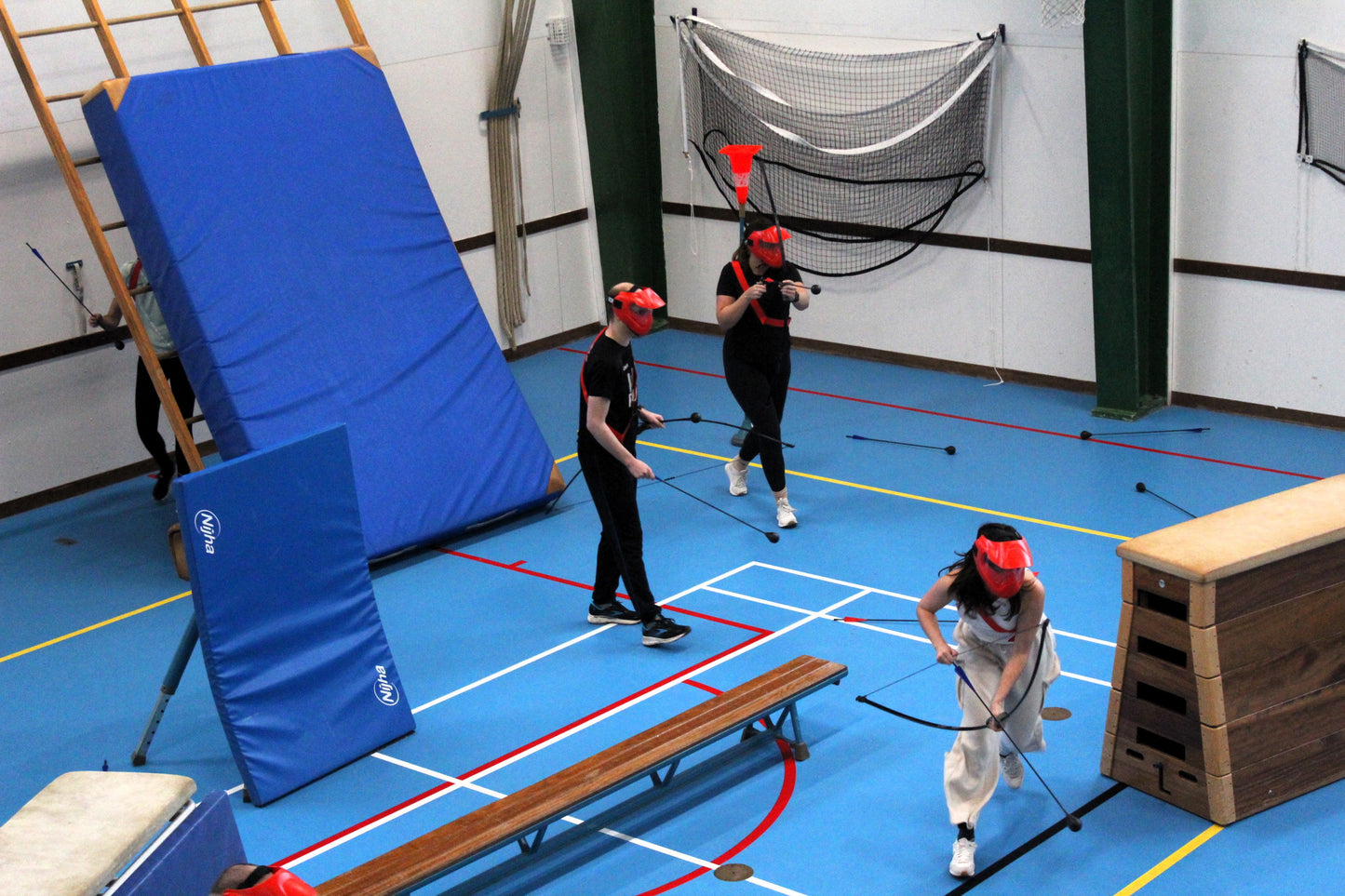Indoor sports facility with blue mats, teamsport, and people practicing archery games