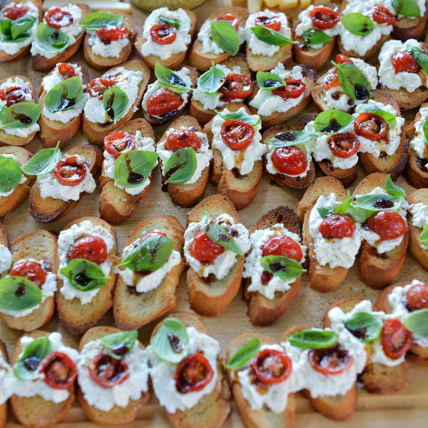 Platter of crostini with ricotta, tomatoes, and basil on a wooden board.