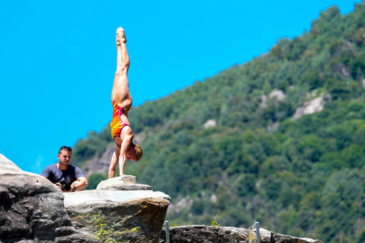 Person performing a handstand on a rock with a scenic background of mountains and clear sky.