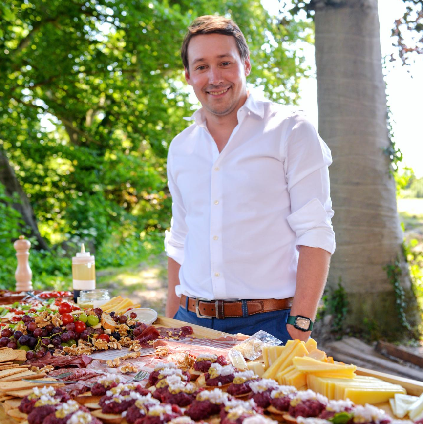 Man standing behind a charcuterie board outdoors with trees in the background