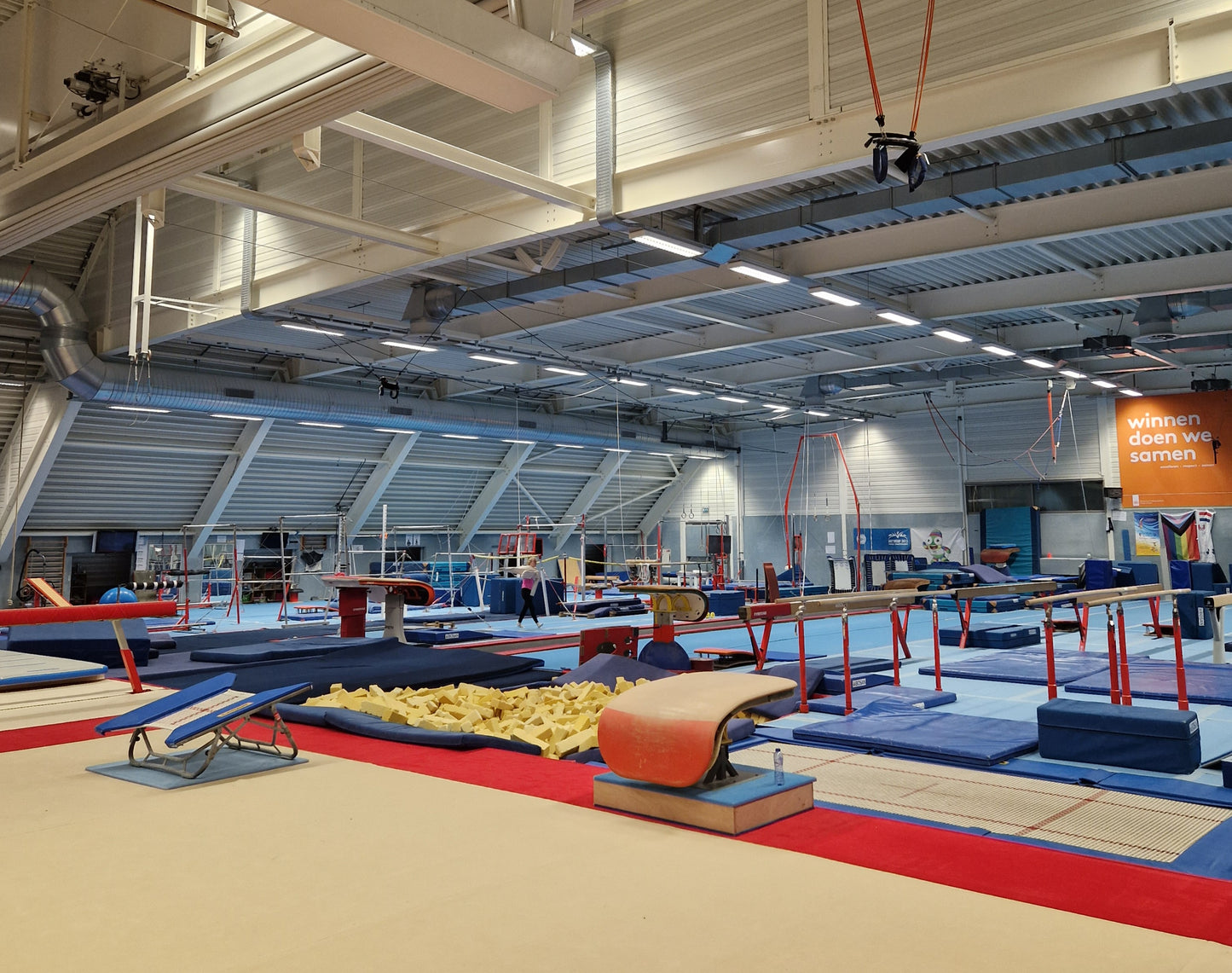 Gymnastics training facility with various equipment and a high ceiling.
