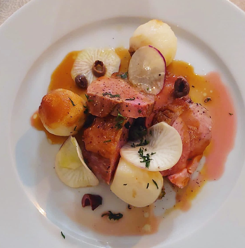 Plated dish with sliced radishes, tomatoes, and other vegetables on a white plate.