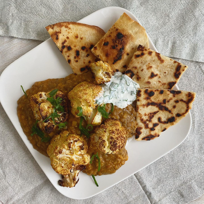 Plated dish of roasted cauliflower with naan bread and a dollop of yogurt sauce on a gray textured surface.
