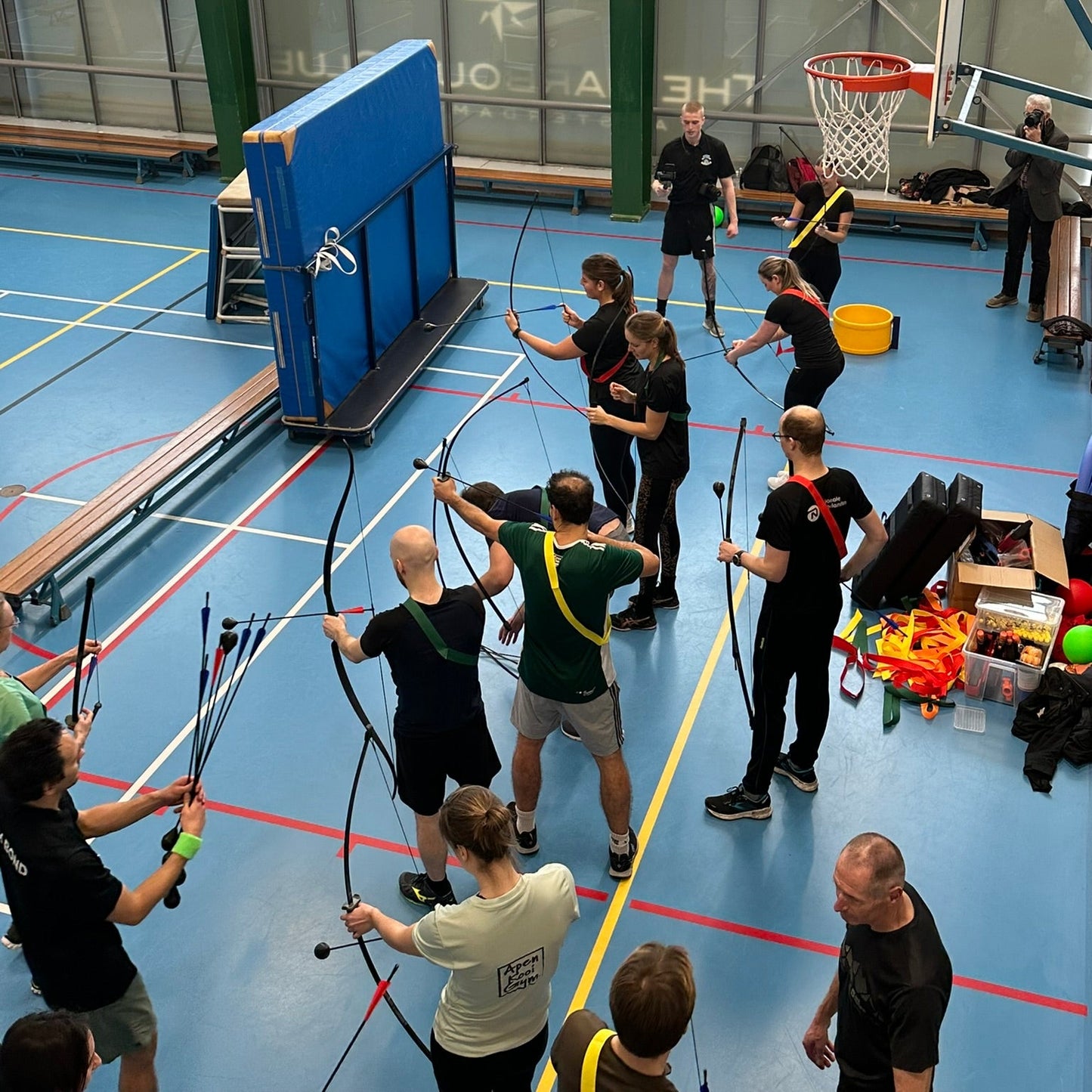 Group of people practicing archery in a gymnasium, without masks