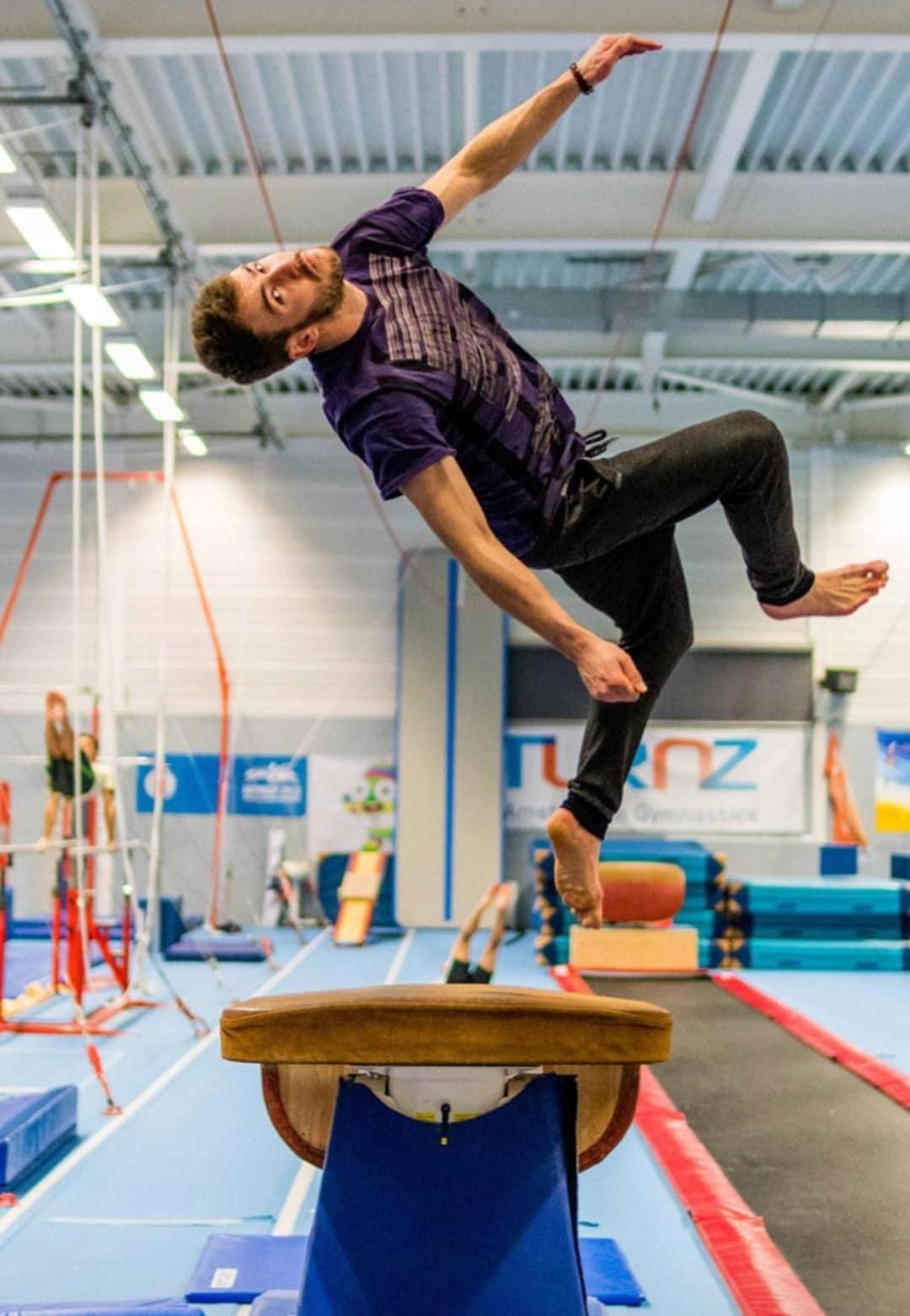 Person performing a gymnastics routine on a balance beam in an indoor sports facility.