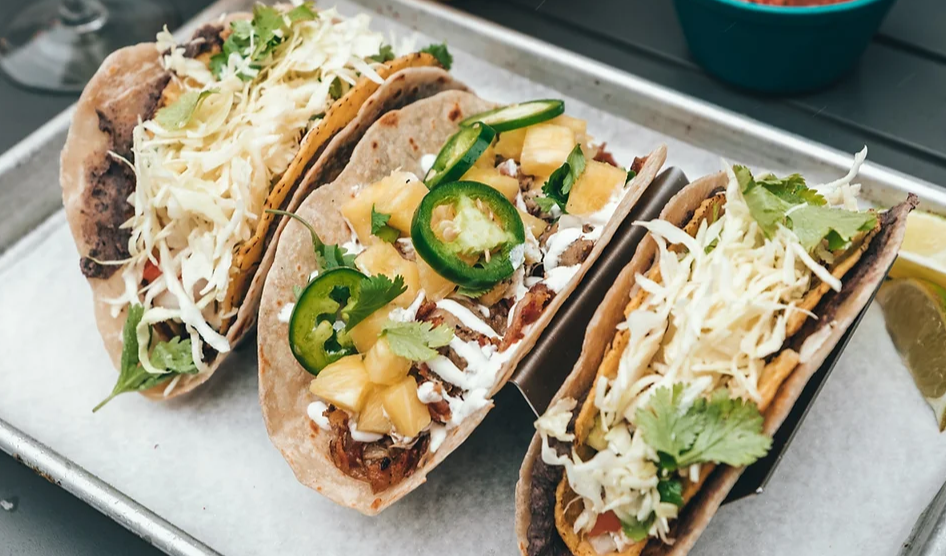 Three tacos with various toppings on a metal tray.