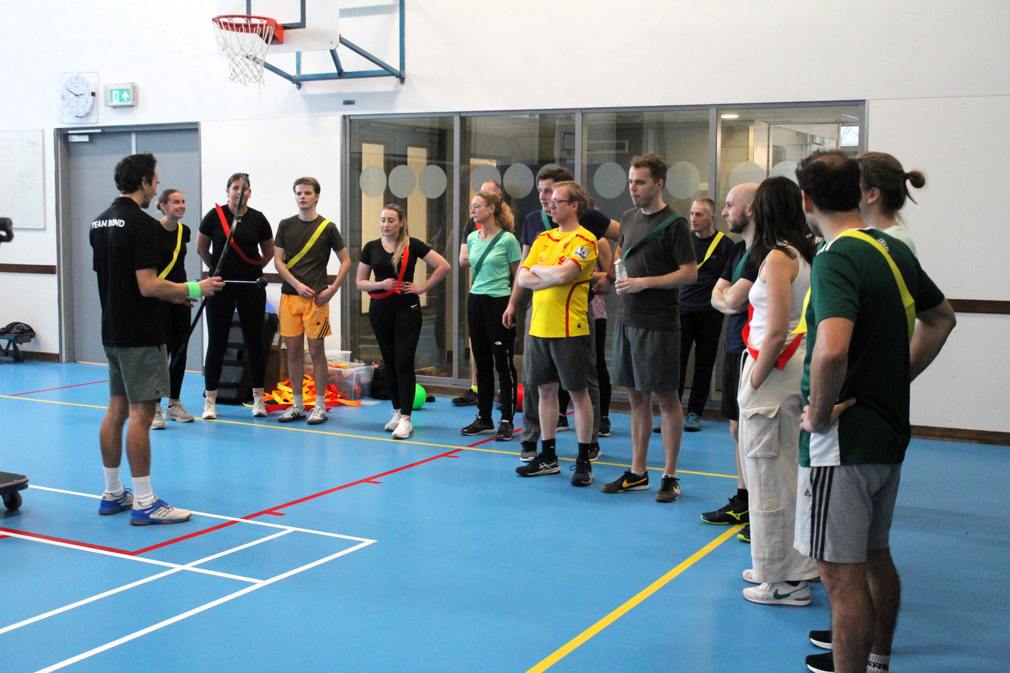 uitleg aan een groep mensen in gymzaal, met het spel apenkooien en archery tag