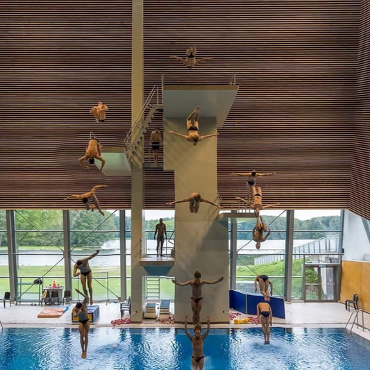 Person diving into a pool from a high dive platform with a scenic background.